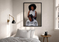 Hair Braiding Scene with Two Figures print in a black frame above a bed with striped linens