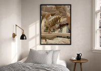 Hair Claw and Cosmetic Tube print in a black frame above a bed with striped linens, a brass wall lamp and a sunlit window