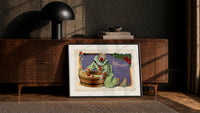 Clown bobbing for apples print in a black frame leaning against a walnut console in lamplight
