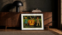 Two children carrying jack-o-lantern pumpkin print in a black frame leaning against a walnut console in lamplight