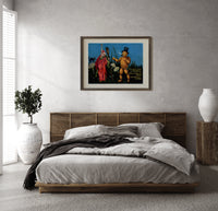 Witch and pumpkin man walking print in a dark wood frame above a rattan bed on a plaster wall