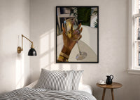 Raised Wine Glass print in a black frame above a bed with striped linens, a brass wall lamp and a sunlit window
