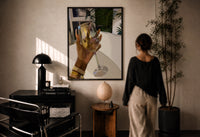 Raised Wine Glass print in a black frame on a sunlit plaster wall, a woman looking on beside a mushroom lamp
