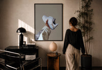 White Sneaker with Gold Chains print in a black frame on a sunlit plaster wall, a woman looking on beside a mushroom lamp