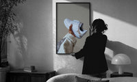 White Sneaker with Gold Chains print in a slim black frame being hung on a sunlit wall in a monochrome room
