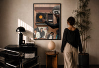Hand on a Wooden Record Player print in a black frame on a sunlit plaster wall, a woman looking on beside a mushroom lamp
