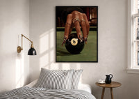 Hand on the Eight Ball print in a black frame above a bed with striped linens, a brass wall lamp and a sunlit window