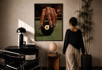 Hand on the Eight Ball print in a black frame on a sunlit plaster wall, a woman looking on beside a mushroom lamp