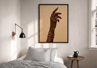 Hand with a Cross and Gold Chains print in a black frame above a bed with striped linens