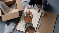 Hand with Blue Bangles framed print being unpacked from protective bubble wrap and a box