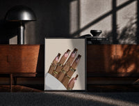 Black-framed Hand with Brown Swirl Nails print on the floor in front of a dark wooden console