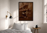Gold Cross Necklace print in a black frame above a bed with striped linens, a brass wall lamp and a sunlit window
