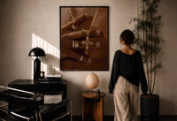 Gold Cross Necklace print in a black frame on a sunlit plaster wall, a woman looking on beside a mushroom lamp