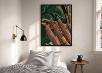 Green French Tips print in a black frame above a bed with striped linens, a brass wall lamp and a sunlit window