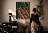 Green French Tips print in a black frame on a sunlit plaster wall, a woman looking on beside a mushroom lamp