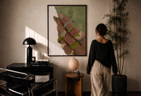Hand with Green Nails and Rings print in a black frame on a sunlit plaster wall, a woman looking on beside a mushroom lamp