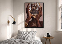 Hands Holding an Ornate Mirror print in a black frame above a bed with striped linens, a brass wall lamp and a sunlit window