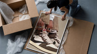 Hands Lacing Brown High-Tops framed print being unpacked from protective bubble wrap and a box