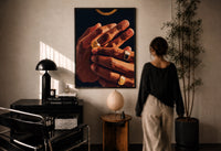 Hands with Gold Rings print in a black frame on a sunlit plaster wall, a woman looking on beside a mushroom lamp