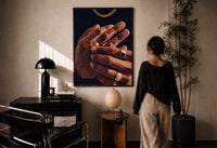 Hands with Gold Rings on Navy print in a black frame on a sunlit plaster wall, a woman looking on beside a mushroom lamp