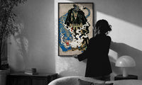 Hannya mask samurai beside a blue tiger print in a slim black frame being hung on a sunlit wall in a monochrome room