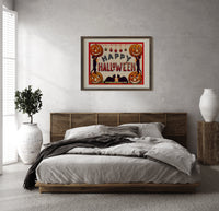 Halloween jack-o-lanterns and black cats print in a dark wood frame above a rattan bed on a plaster wall