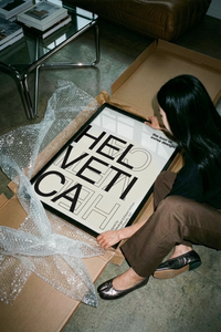 Woman lifting a Helvetica Swiss typography wall art print out of a brown cardboard shipping tube