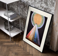 Golden sun with pyramid of colors poster in a black frame leaning beside a shelf in a raw-plaster loft