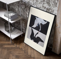 Two swans, one white one black poster in a black frame leaning beside a shelf in a raw-plaster loft