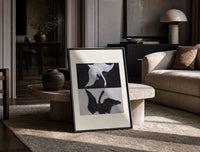 Two swans, one white one black print in a black frame leaning on a travertine table in a sunlit lounge