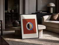 Divided circle with concentric rings print in a black frame leaning on a travertine table in a sunlit lounge