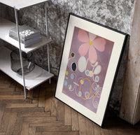 Abstract flower with swirls and circles poster in a black frame leaning beside a shelf in a raw-plaster loft