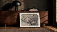Travelers in rainstorm on hillside path print in a black frame leaning against a walnut console in lamplight