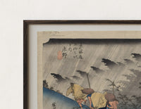 Close-up of the Travelers in rainstorm on hillside path print's dark wood frame corner and archival matte paper