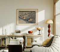 Travelers in rainstorm on hillside path print in an oak frame above a mid-century book console with a vintage radio