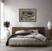 Snowy Japanese village travelers at night print in a dark wood frame above a rattan bed on a plaster wall