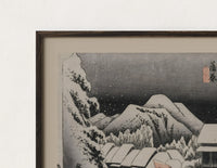 Close-up of the Snowy Japanese village travelers at night print's dark wood frame corner and archival matte paper