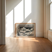Snowy Japanese village travelers at night print in an oak frame on a sunlit wood floor beneath tall window light