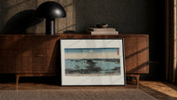 Japanese bay landscape with moon print in a black frame leaning against a walnut console in lamplight