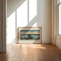 Japanese bay landscape with moon print in an oak frame on a sunlit wood floor beneath tall window light