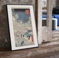 Snowy bridge with travelers in winter print in a black frame leaning beside a vintage door on parquet