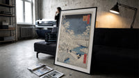 Snowy bridge with travelers in winter print in a slim black frame leaning on a dark sofa in a concrete print studio