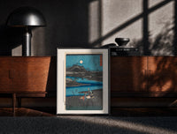 Black-framed Women washing cloth by moonlit river print on a moody console with designer coffee-table books