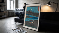 Women washing cloth by moonlit river print in a slim black frame leaning on a dark sofa in a concrete print studio