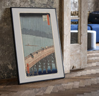 People crossing bridge in rain print in a black frame leaning beside a vintage door on parquet