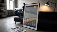 People crossing bridge in rain print in a slim black frame leaning on a dark sofa in a concrete print studio