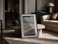 People crossing bridge in rain print in a black frame leaning on a travertine table in a sunlit lounge