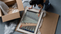 People crossing bridge in rain framed print being unpacked from protective bubble wrap and a box