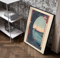River landscape with plum blossom branch poster in a black frame leaning beside a shelf in a raw-plaster loft
