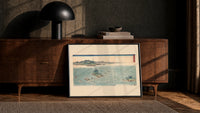 Japanese whirlpools and coastal seascape print in a black frame leaning against a walnut console in lamplight